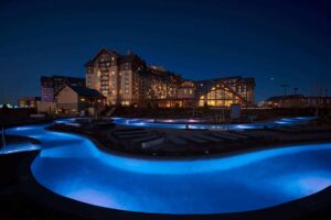 Large resort style pool illuminated with blue lighting at night with lodge in background