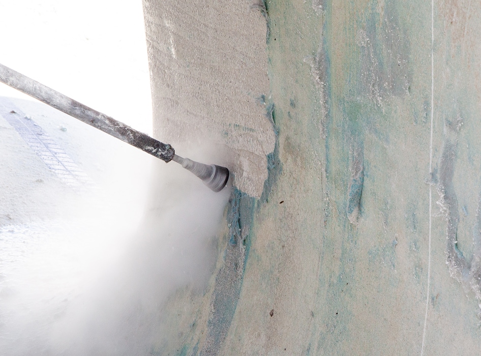 A high-pressure water jet sprays against a textured concrete surface, removing dirt and grime. Mist and droplets convey a sense of action and intensity.