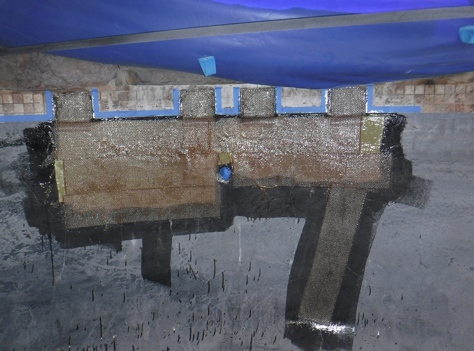 Concrete wall with repair work featuring patches of dark and light materials, possibly for water sealing. A blue tarp partially covers the top.