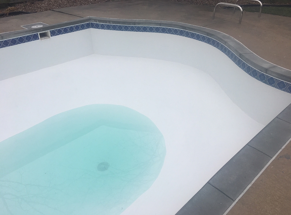 Empty white pool with a small section filled with light blue water, surrounded by a blue patterned tile border. Atmosphere is calm and minimalist.
