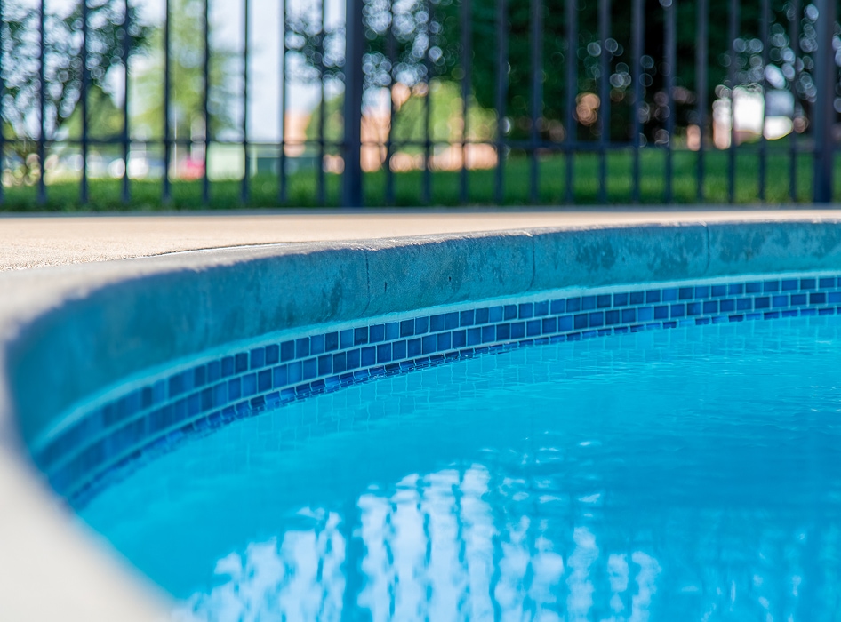 Close up of pool edge with blue tiles water reflection and black metal fence in background