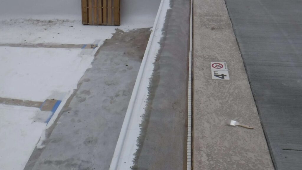 An empty swimming pool under construction shows a partially tiled edge with a "4 ft" depth marker and a small paintbrush lying on the concrete.