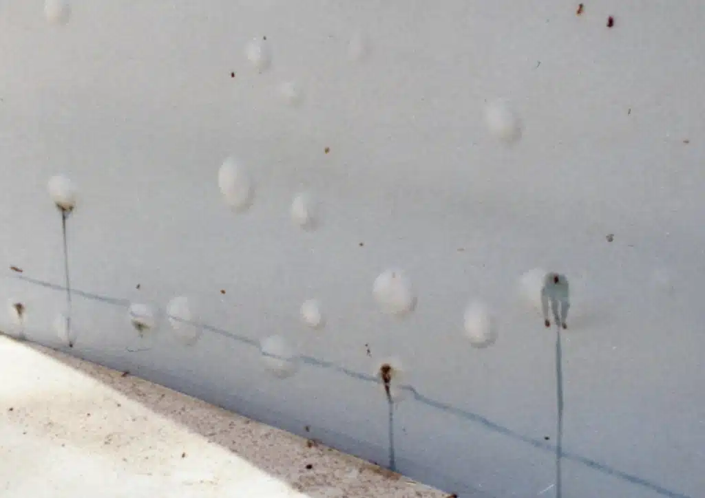 Close-up of a white wall showing multiple small paint bubbles and thin, dark streaks of water damage, conveying a sense of aging and decay.