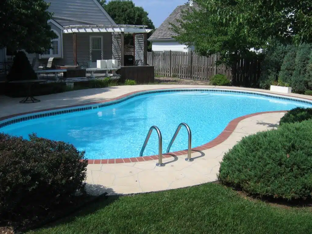 Standard residential swimming pool with curved shape, metal ladder, and patio area — backyard pool renovation and design inspiration