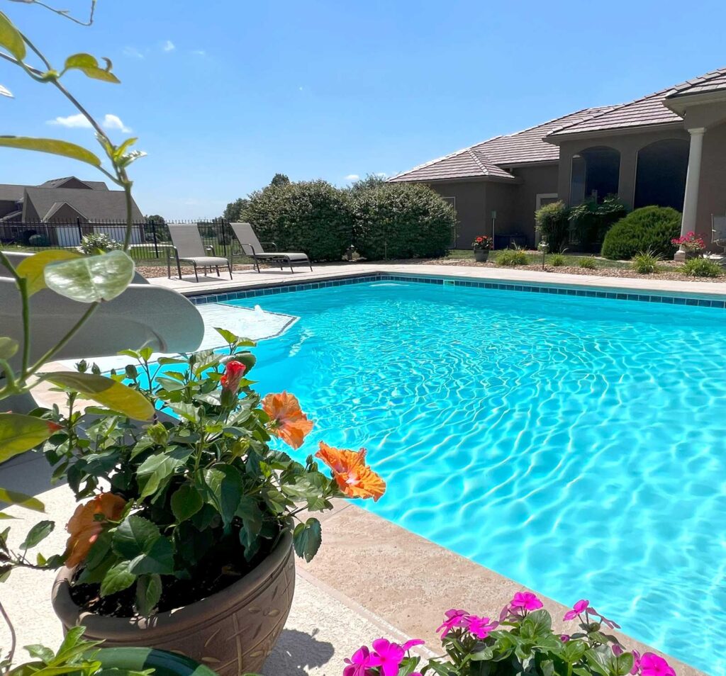 Outdoor pool with vibrant flowers in foreground and residential backdrop — decorative pool landscaping and renovation