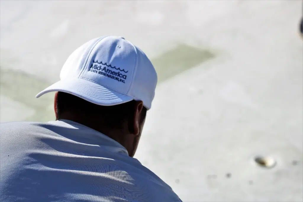 A person wearing a white cap with "Mid-America Pool Renovations, Inc." faces a bright, sunlit surface. The scene conveys focus and calmness.