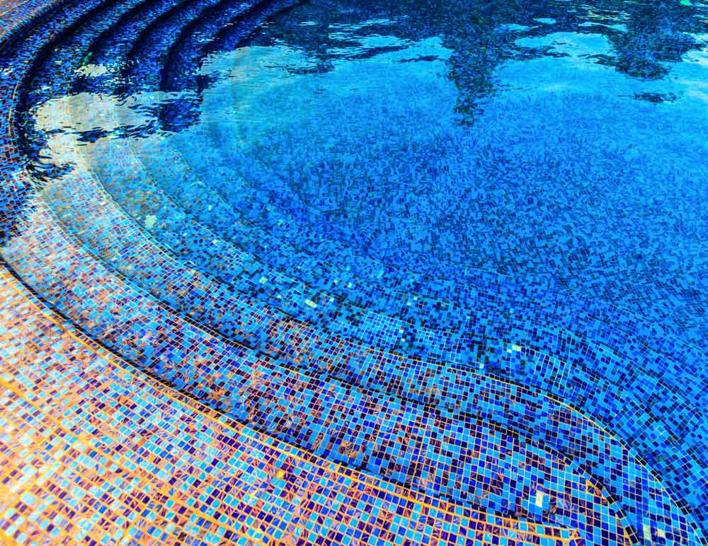 Close‑up of swimming pool interior with vibrant blue mosaic tiles and water reflections — decorative pool tiling and renovation inspiration