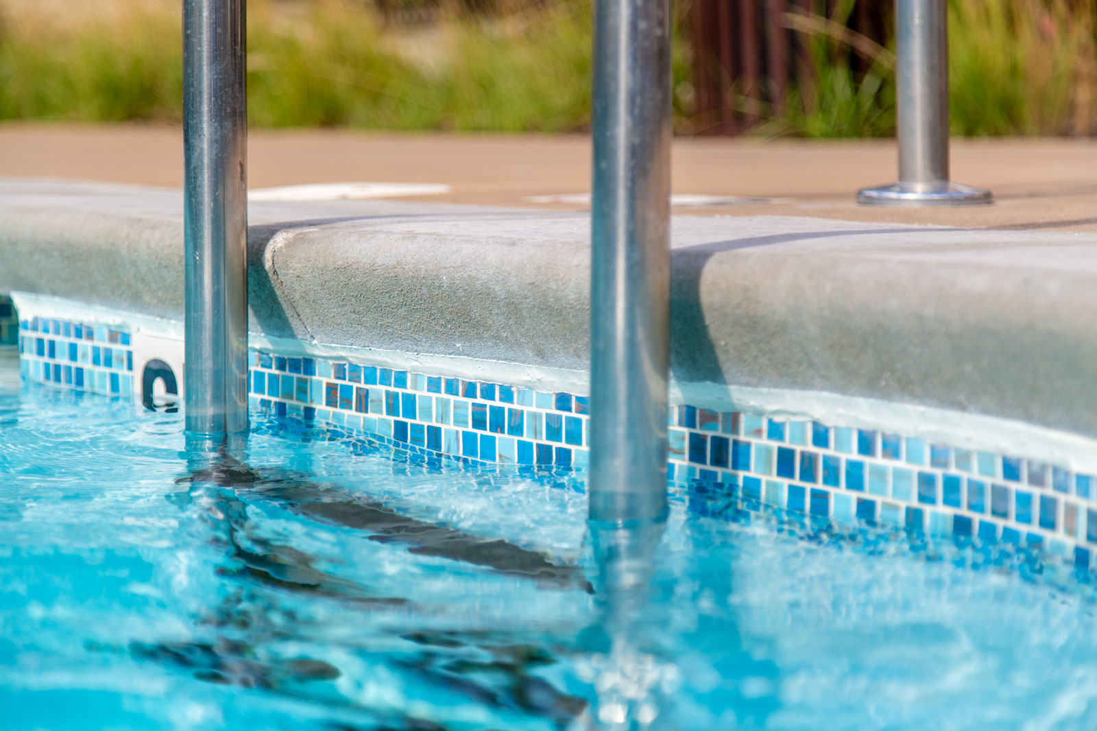 Close-up of pool edge with metal handrail and decorative blue tiles — poolside renovation and tile installation.