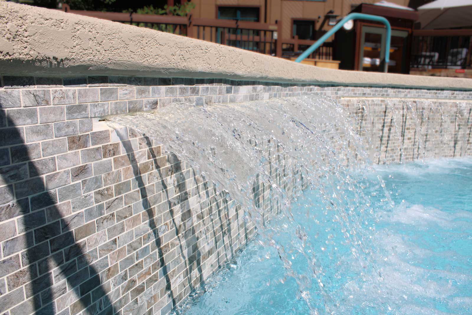 Cascading water feature beside swimming pool — pool landscaping and decorative renovation