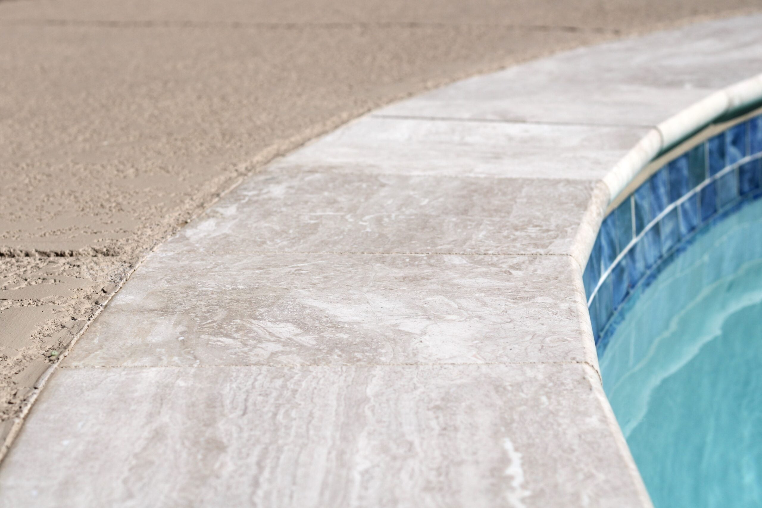 Close-up of pool edge showing textured stone or tile deck surface — pool deck material and renovation detail