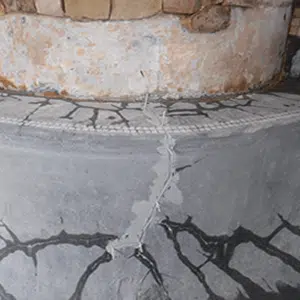 A close-up of a weathered, cracked stone structure with visible lines of repair. The surface shows signs of age and texture, conveying durability and history.