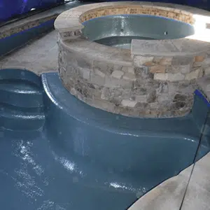 A partially finished stone hot tub with a smooth, blue concrete interior. Curved steps lead to the tub, suggesting an ongoing construction project.