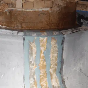 A rustic stone oven with a worn blue and white painted chimney reflects age and history. The texture suggests a weathered, vintage ambiance.
