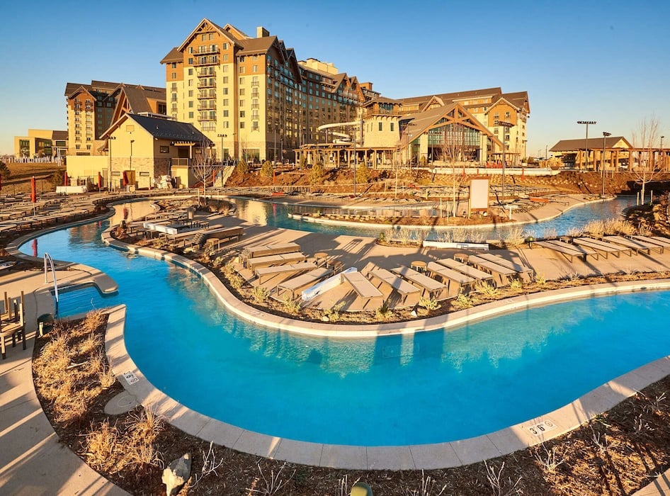 Luxurious hotel with a spa-like atmosphere, featuring a large outdoor pool under a bright sky. Modern architecture with glass, wood, and stone elements.