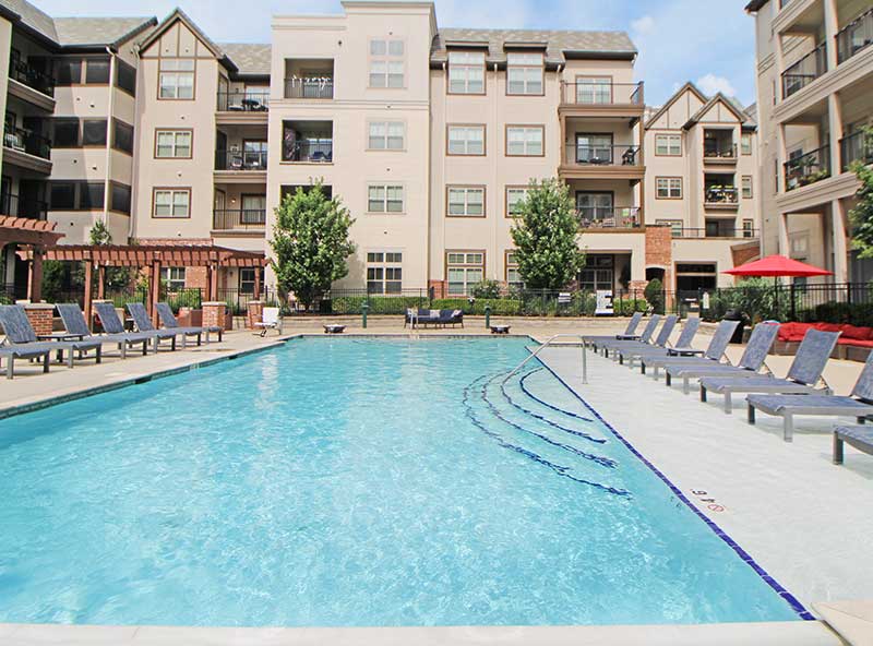 Swimming pool beside apartment complex with lounge chairs — residential pool renovation and community amenities.
