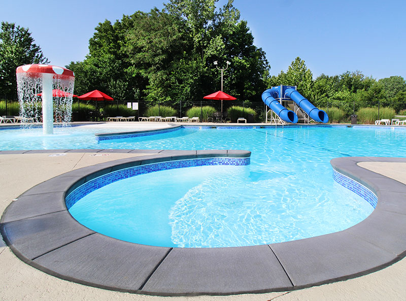 Outdoor pool with circular hot tub surrounded by trees and red umbrellas — residential pool and spa design.