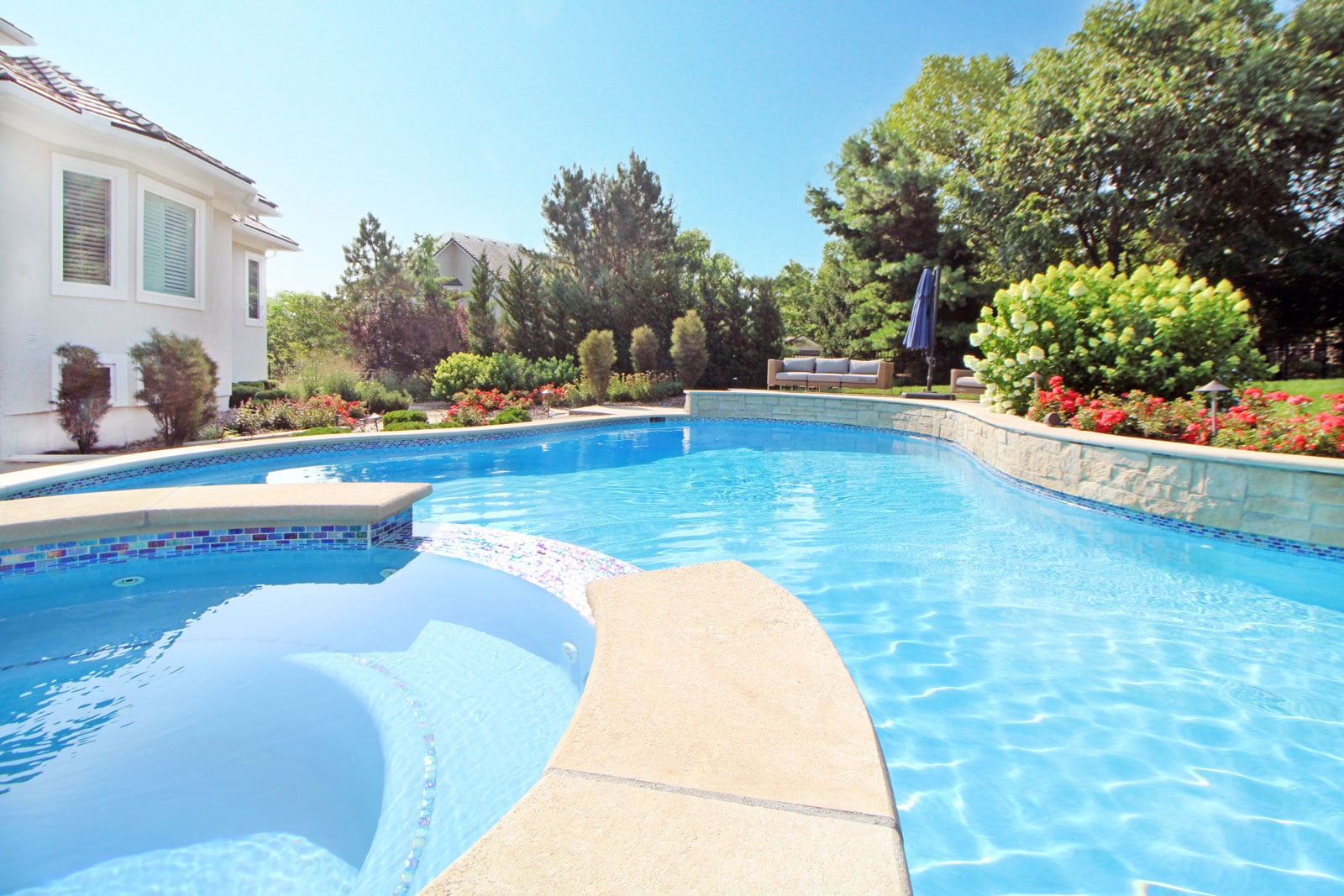 Residential outdoor swimming pool with clear blue water and landscaped seating — backyard pool design and renovation.