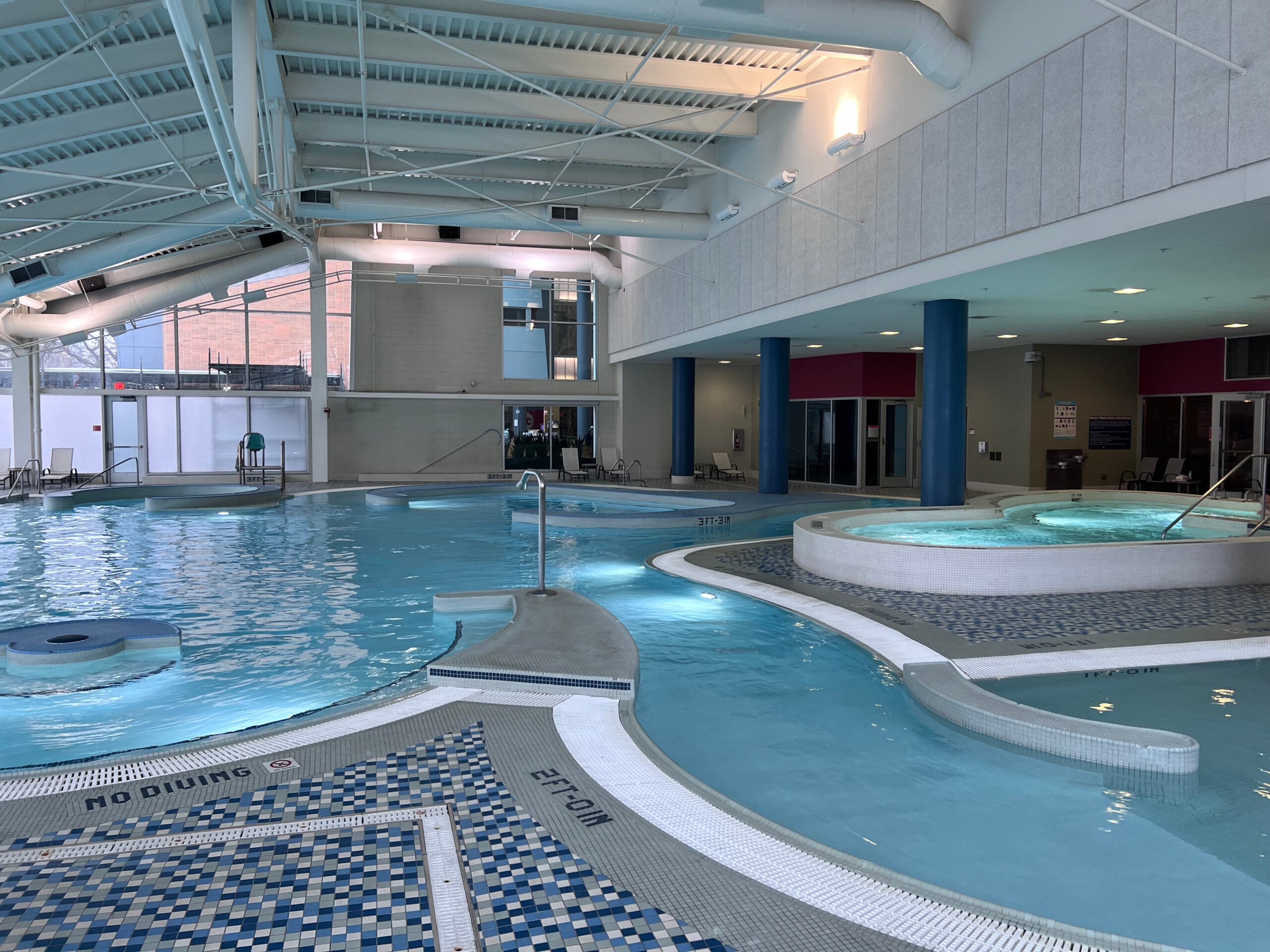 An indoor swimming pool area with various sections including a larger pool, hot tubs, and tiled flooring.