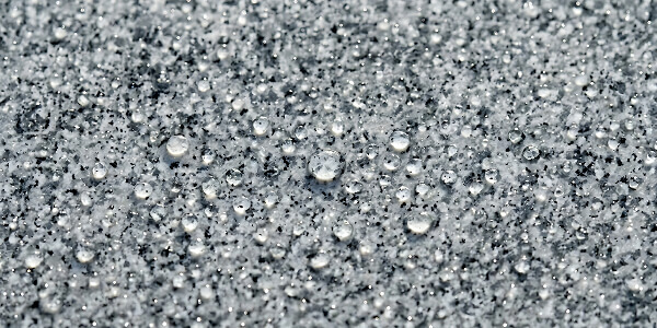 Close-up of numerous small water droplets on a smooth, gray surface, creating a textured effect. The droplets vary in size, evoking a fresh, cool atmosphere.