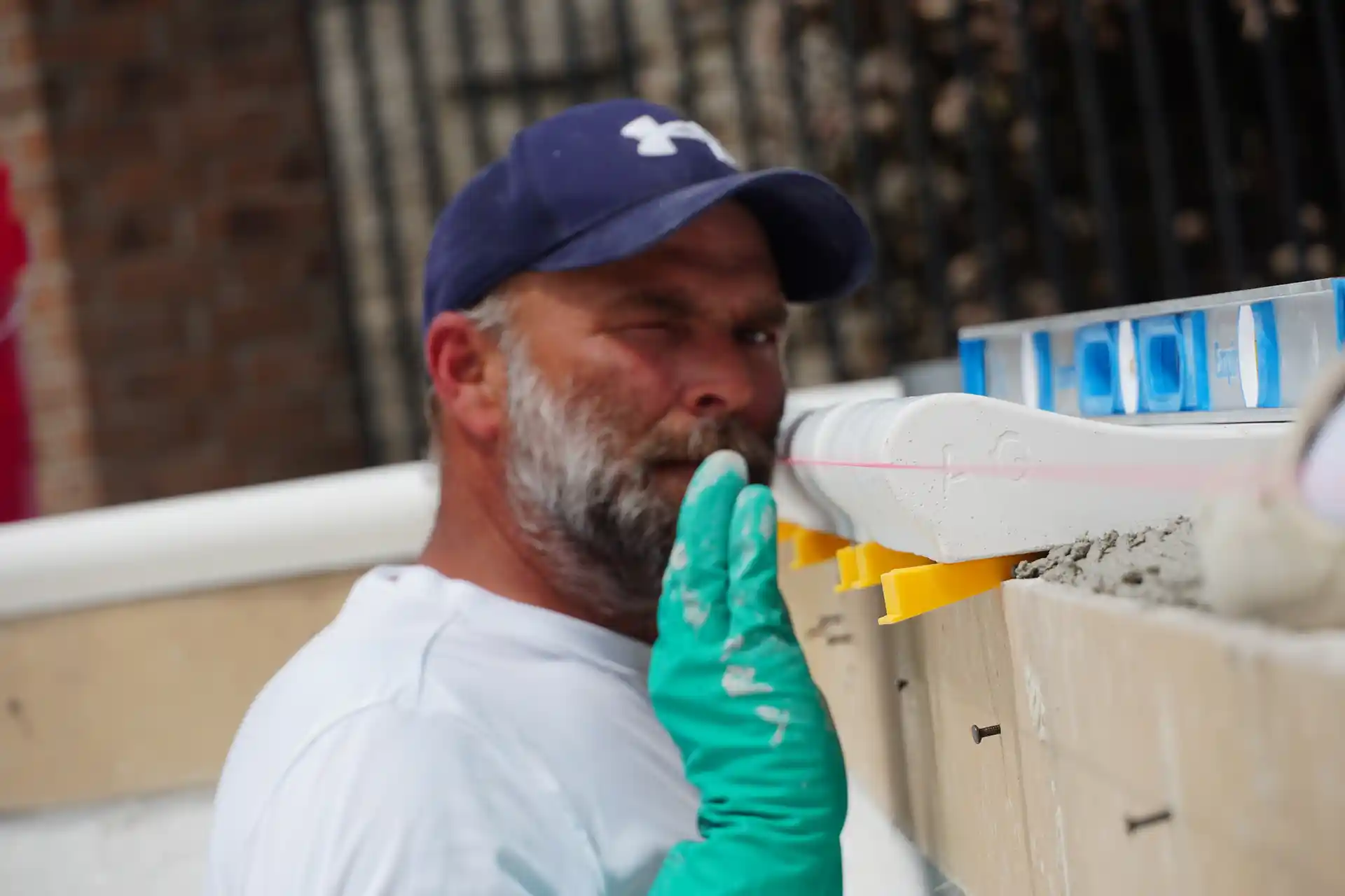 A man wearing a blue cap and gloves, working with a construction project, focusing on a measurement or alignment task.