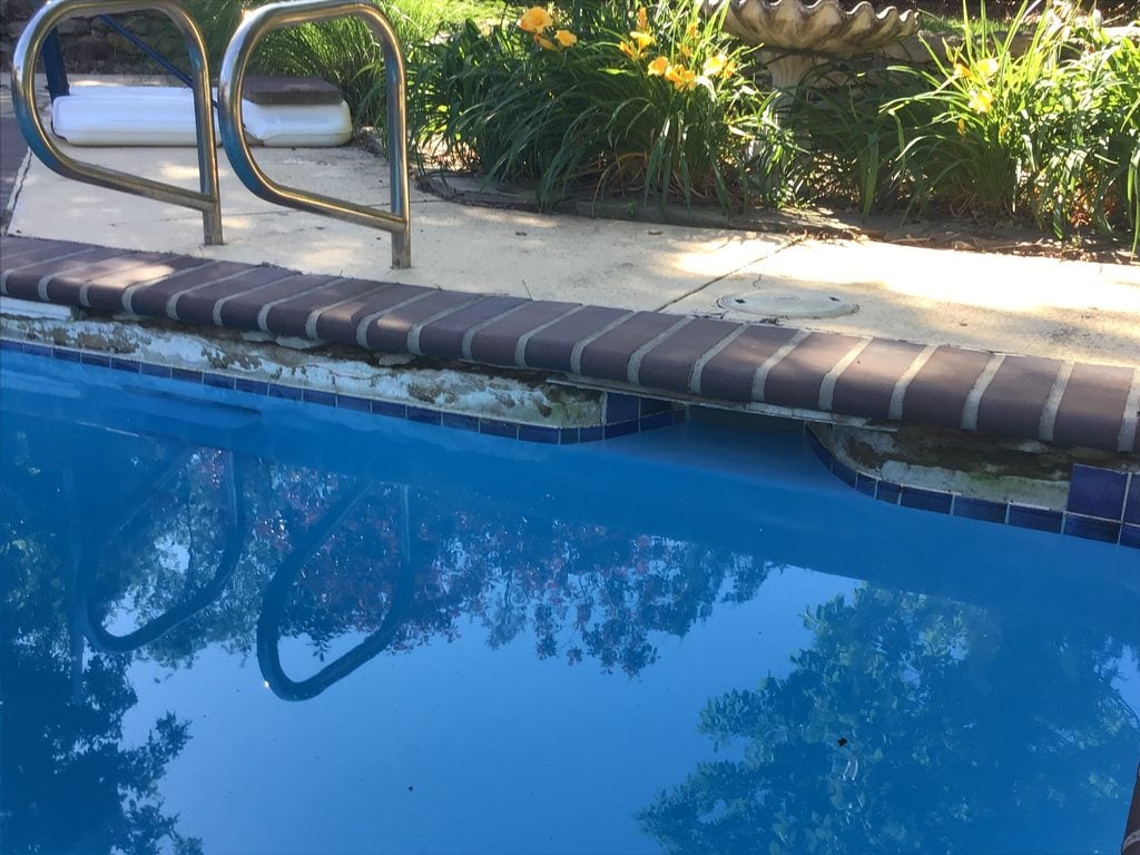 A filled swimming pool with blue water shows deterioration along the waterline