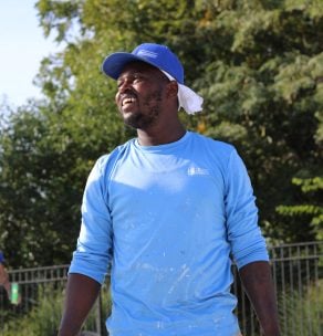 Person in light blue shirt and cap outdoors near fence and trees — pool inspection and supervision service