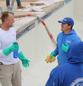 Three workers performing maintenance on empty swimming pool — professional pool cleaning and chemical treatment service